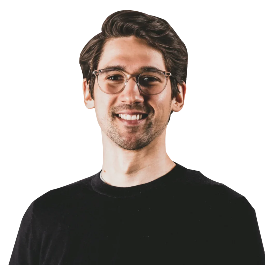 Extendly CRM - Een jonge man met golvend bruin haar, bril en gezichtshaar glimlacht terwijl hij een zwart shirt draagt tegen een effen, lichte achtergrond.